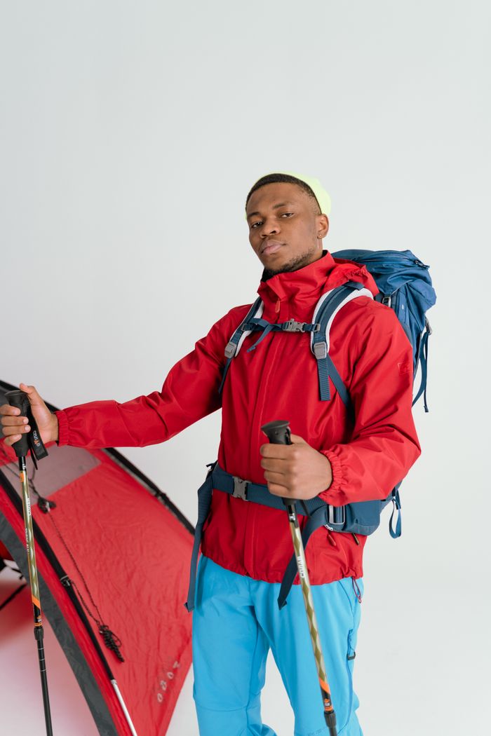 Home Portrait of a hiker in a red jacket with tent and trekking poles.